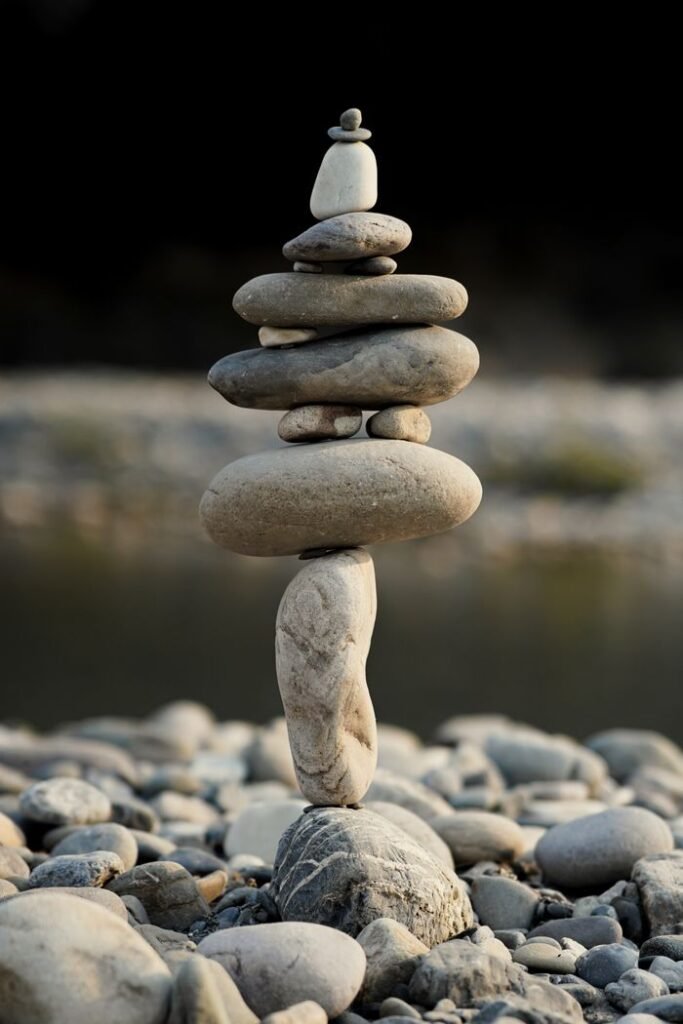 Vous êtes un particulier A vertical stack of smooth stones balancing by a tranquil riverside, symbolizing peace and harmony.
